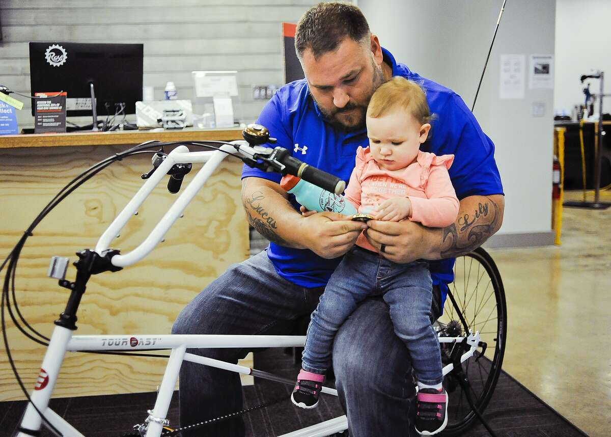 Adam Morton of Saginaw sits on his brand new recumbent bike with his daughter Brinlee, 14 months, on Wednesday, April 10, 2019 at Ray's Bike Shop in Midland. Morton is a veteran, and while serving in Iraq an explosion left him with debilitating injuries to his back and right leg, making it much too painful to use a regular bike. Morton received the bike through the Buddy to Buddy program, with a donation from The Fallen and Wounded Soldiers Fund. (Katy Kildee/kkildee@mdn.net)