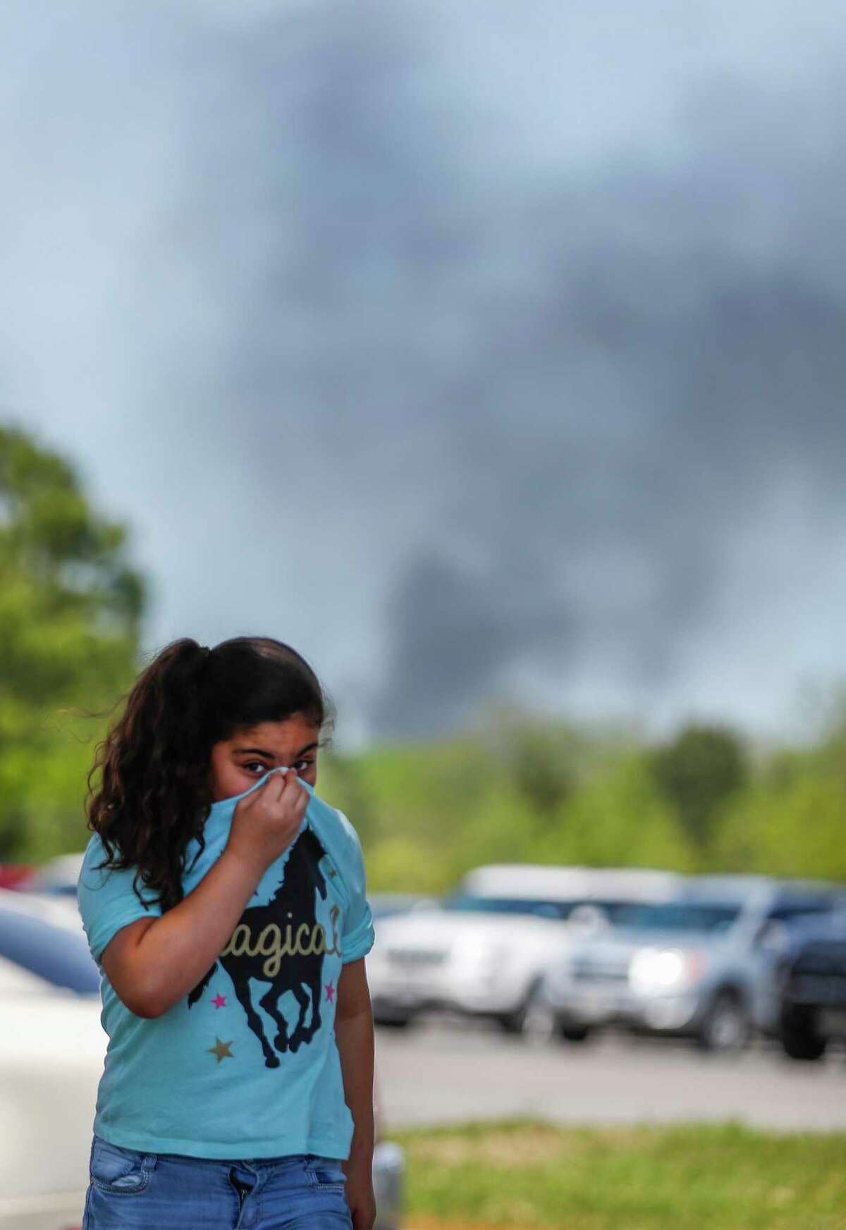A little girl covers her nose as she and her family came to pick up a family member from the Crosby Kindergarten Center as the plume from the KMCO fire, billowed in the backround, Tuesday, April 2, 2019, in Crosby.