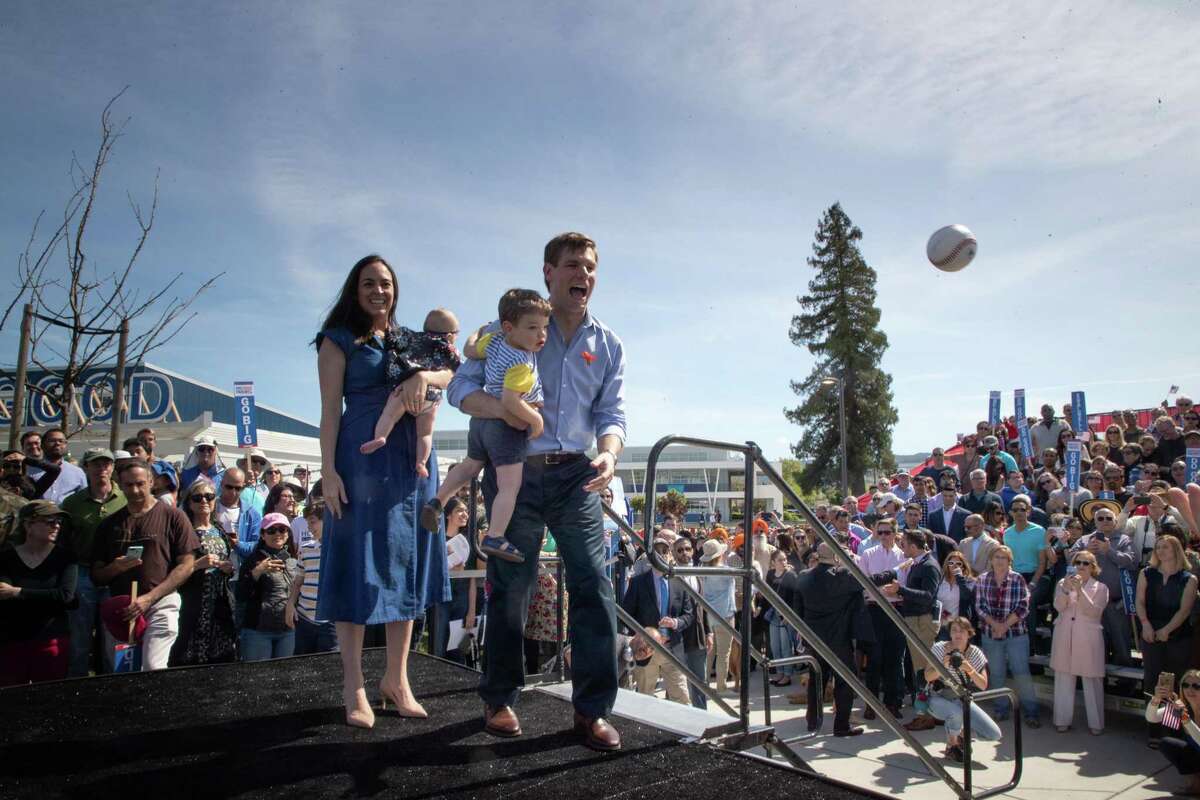Swalwell tosses a signed ball back to a supporter while his 1-year-old son, Nelson, cries to keep it. With him is his wife, Brittany, carrying 5-month-old Kathryn.