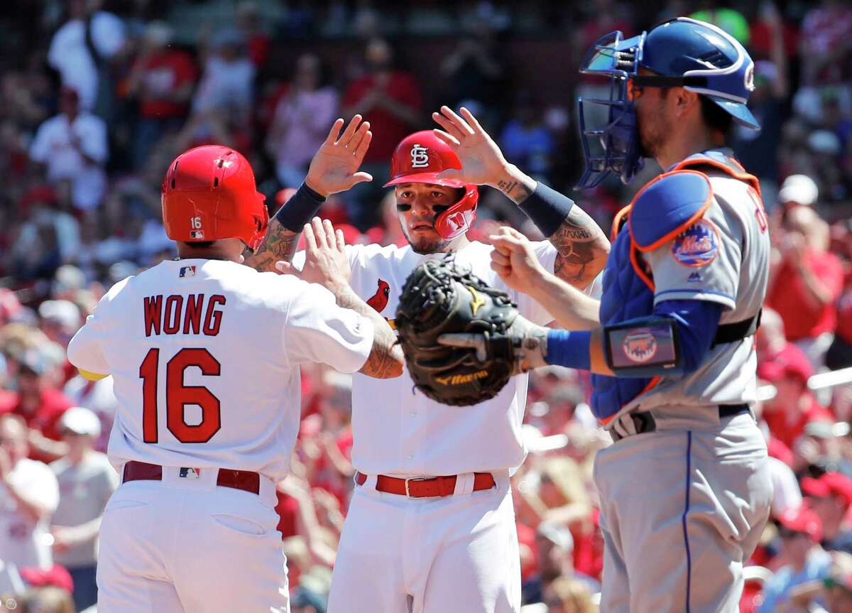 St. Louis Cardinals' Kolten Wong, left, and teammate Yadier Molina celebrate after scoring past New York Mets catcher Travis d'Arnaud, right, during the second inning of a baseball game Sunday, April 21, 2019, in St. Louis. (AP Photo/Jeff Roberson)
