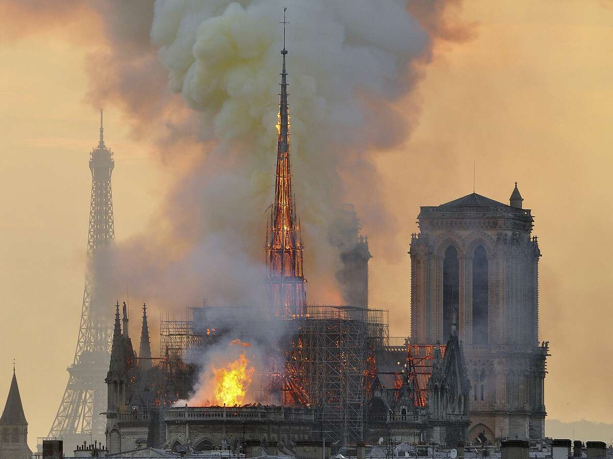 FILE - In this file photo dated Monday, April 15, 2019, with the Eiffel Tower behind, left, flames and smoke rise from the blaze at Notre Dame Cathedral in Paris that destroyed its spire and its roof but spared its twin medieval bell towers, and prompted a frantic rescue effort to save its most precious artefacts. The recent devastating Notre Dame fire in Paris was a warning bell that all of Europe needs to hear, since so many monuments and palaces across the continent are in need of better upkeep according to European officials. “We are so used to our outstanding cultural heritage in Europe that we tend to forget that it needs constant care and attention,” Tibor Navracsics, the European Union’s top culture official, told The Associated Press. (AP Photo/Thierry Mallet, FILE)