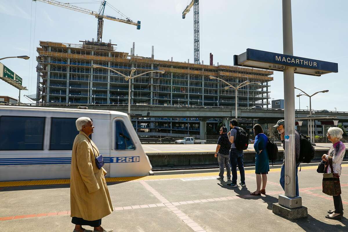 People wait to board the BART at the MacArthur BART station while an apartment building is seen under construction in Oakland.