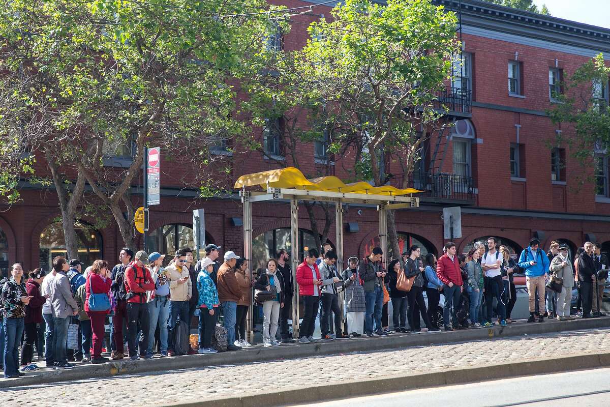 People stand at a bus stop at Market and Church Street waiting for shuttle buses headed downtown. After a power line failure commuters had to take alternative route to get to their destinations. on Friday, April 26, 2019. San Francisco, Calif.