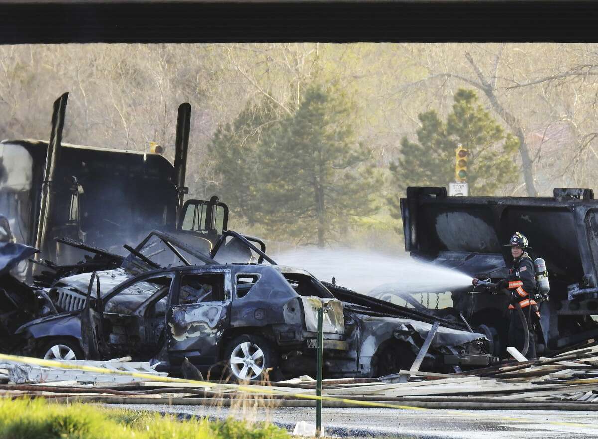 In this Thursday, April 25, 2019 photo, a firefighter sprays water on the wreckage in Lakewood, Colo., after a deadly collision on Interstate 70 near the Colorado Mills Parkway. On Friday, police said the truck driver blamed for causing the fatal pileup involving over two dozen vehicles has been arrested on vehicular homicide charges. (Hyoung Chang/The Denver Post via AP)