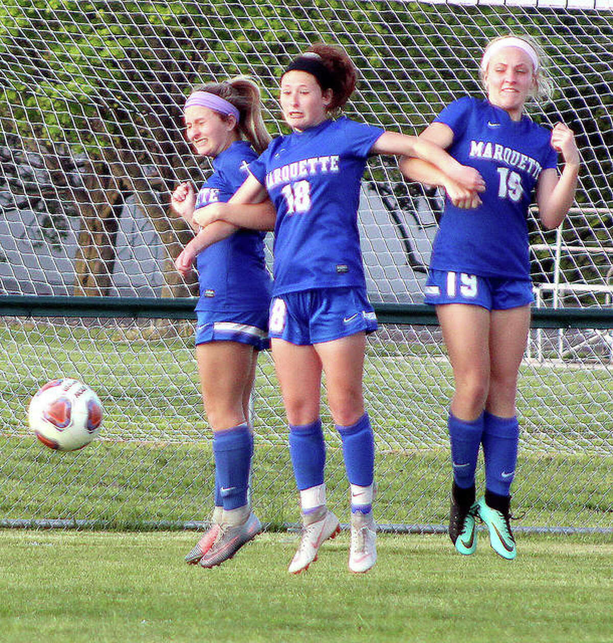 From left, Marquette’s Lydia Randazzo, Madelyn Smith and Amma Anselm leap with arms locked together as they form a defensive wall during a Belleville East free kick late in Monday’s 3-1 Marquette victory at Gordon Moore Park.