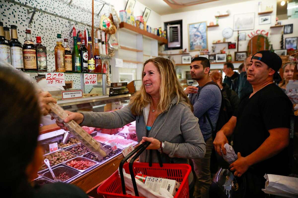 Customer Brenda Weiss passes an item down the line as she waits to check out at Lucca Ravioli's on it's final day open after 90 years of business on Valencia Street in San Francisco, California, on Tuesday, April 30, 2019.