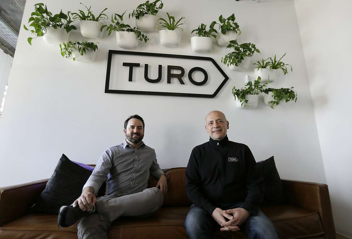 In this April 29, 2019, photo, Steve Webb, VP of Communications, left, and Andre Haddad, CEO, right, pose in the entryway of Turo in San Francisco. Car-sharing apps that let people rent out their vehicles to strangers are growing in popularity in the U.S. But the people who rent cars through apps like Turo and GetAround don’t pay the taxes and surcharges that local governments and airports tack onto traditional rental cars. (AP Photo/Eric Risberg)