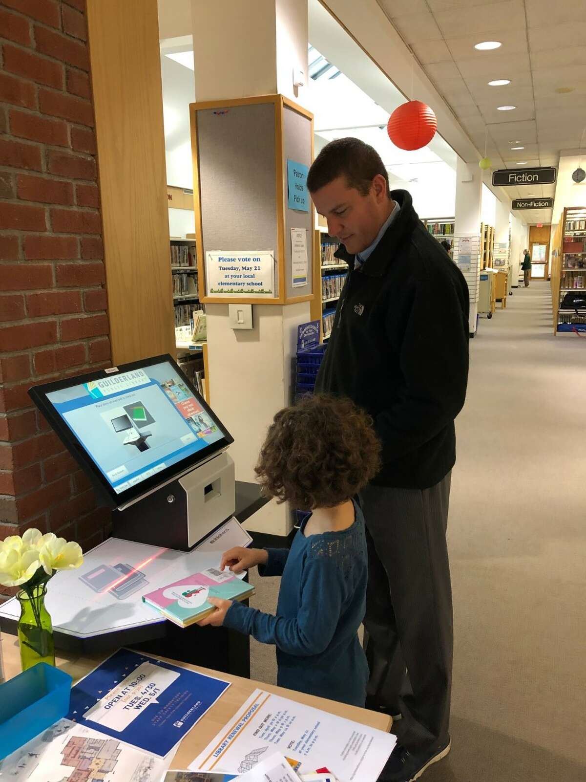 Addison Fisher checks out her children's books while her father, Wade, watches at Guilderland Public Library's self-serve stations. Director Tim Wiles says that since the two stations were installed, 25 percent of all library materials are checked out by patrons via self-service.