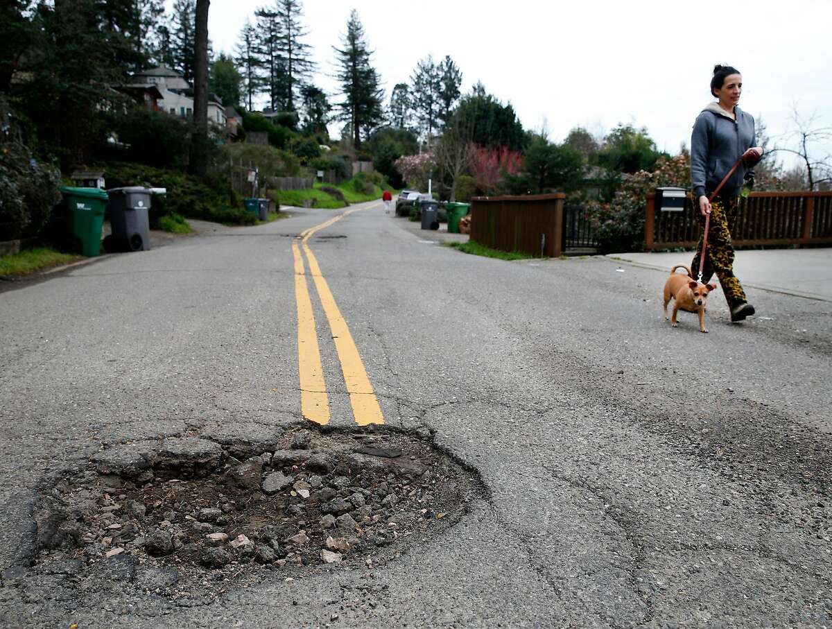 A neighbor walks her dog past a large pothole in the middle of Broadway Terrace in Oakland, Calif. on Wednesday, Feb. 15, 2017. Street maintenance crews are struggling to keep up with a large number of potholes due to the constant rain.
