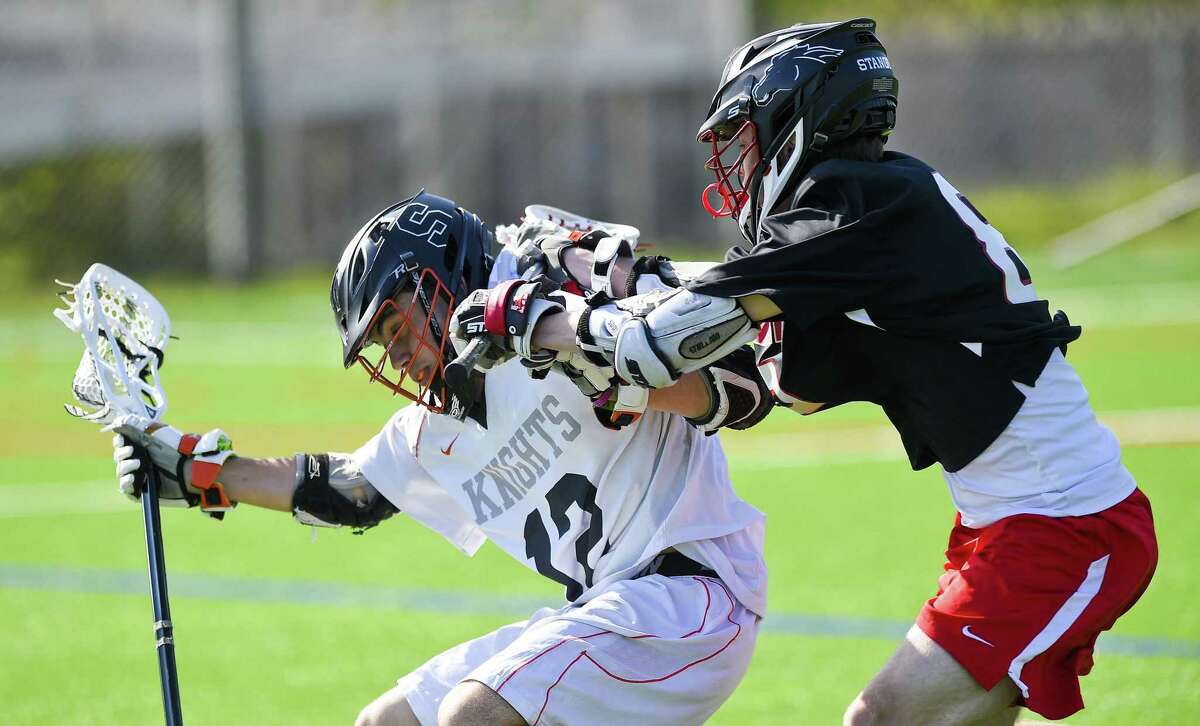 Stamford’s Todd Guttman, left, gets checked by Fairfield Warde’s Witt Badger in the first half of a boys lacrosse game at Stamford High School on Tuesday. Warde defeated Stamford 16-7.