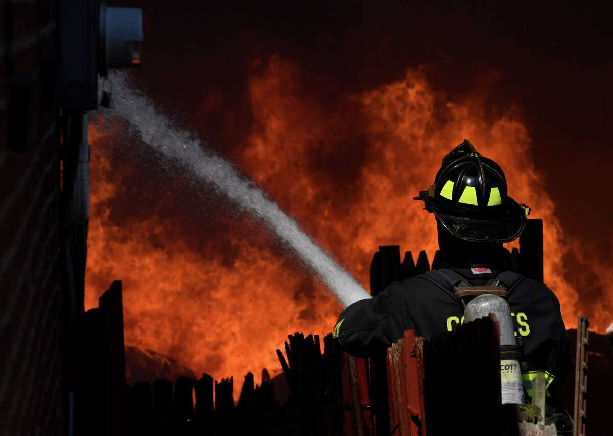 A Cohoes firefighter douses flames that spread to a Sixth Avenue garage from the Alpha Lanes bowling alley fire on Wednesday, May 8, 2019, in Troy, N.Y. (Will Waldron/Times Union)