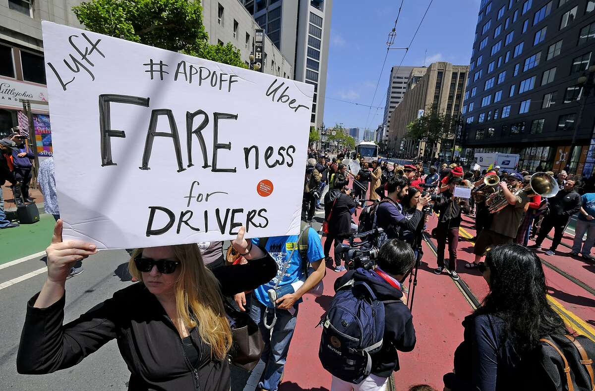 Lyft driver Erica Mighetto, of Sacramento, Calif., holds up a sign as protesters block Market Street outside of Uber headquarters Wednesday, May 8, 2019, in San Francisco. Some drivers for ride-hailing giants Uber and Lyft turned off their apps to protest what they say are declining wages as both companies rake in billions of dollars from investors. Demonstrations in 10 U.S. cities took place Wednesday, including New York, Chicago, Los Angeles, San Francisco and Washington, D.C. The protests take place just before Uber becomes a publicly traded company Friday. (AP Photo/Eric Risberg)