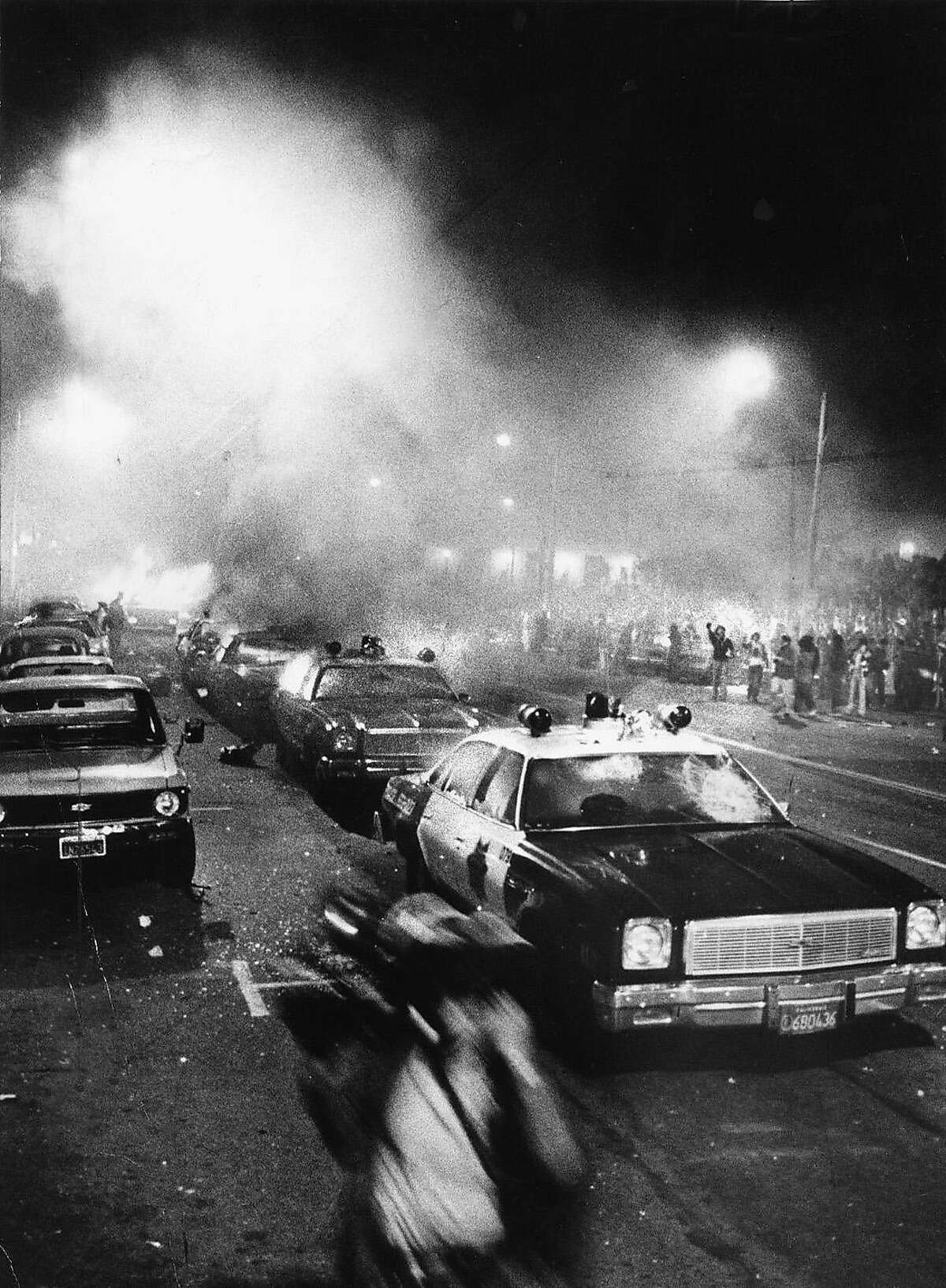 白夜/ 79年5月22日/米/层-市民中心着火的警车整体。前景中的人是一名正在跑步的新闻摄影师。法庭对丹·怀特的判决出来后，骚乱就开始了。骚乱在市政厅附近的市民中心外开始。丹·怀特，乔治·莫斯康，哈维·米尔克。图片来源:JOHN STOREY WHITE NIGHT RIOTS jonestown40