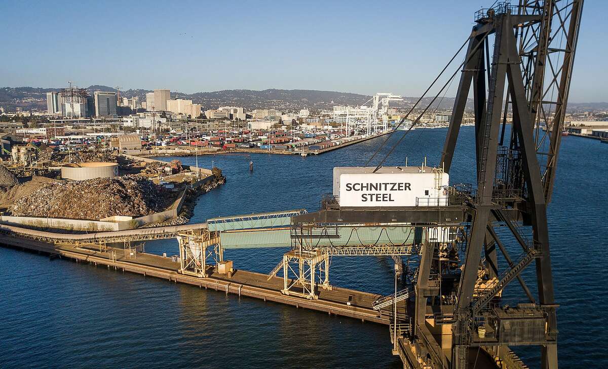 A crane and a conveyor belt rise over the Oakland Estuary at Schnitzer Steel's recycling yard on Monday, Sept. 17, 2018, in Oakland, Calif. Behind the is the Charles P. Howard Terminal which is a proposed location for a new Oakland Athletics ballpark.