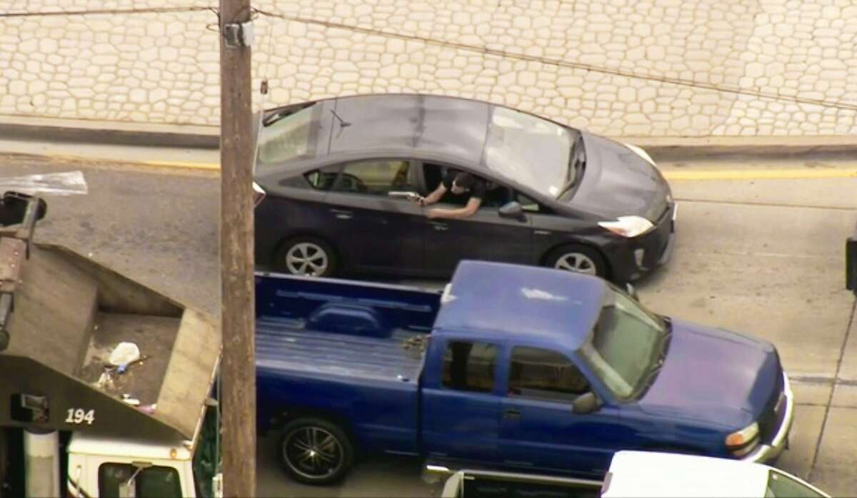 In this photo from video provided by FOX11 Los Angeles shows a man leaning out the window of a moving car, shooting at pursuing police vehicles during a wild car chase in the Los Angeles area Friday afternoon, May 10, 2019. The car finally came to a halt in the Los Angeles suburb of Vernon, where the woman driver, who had blood on her shirt, surrendered. The gunman remained inside the car. (FOX11 Los Angeles via AP)