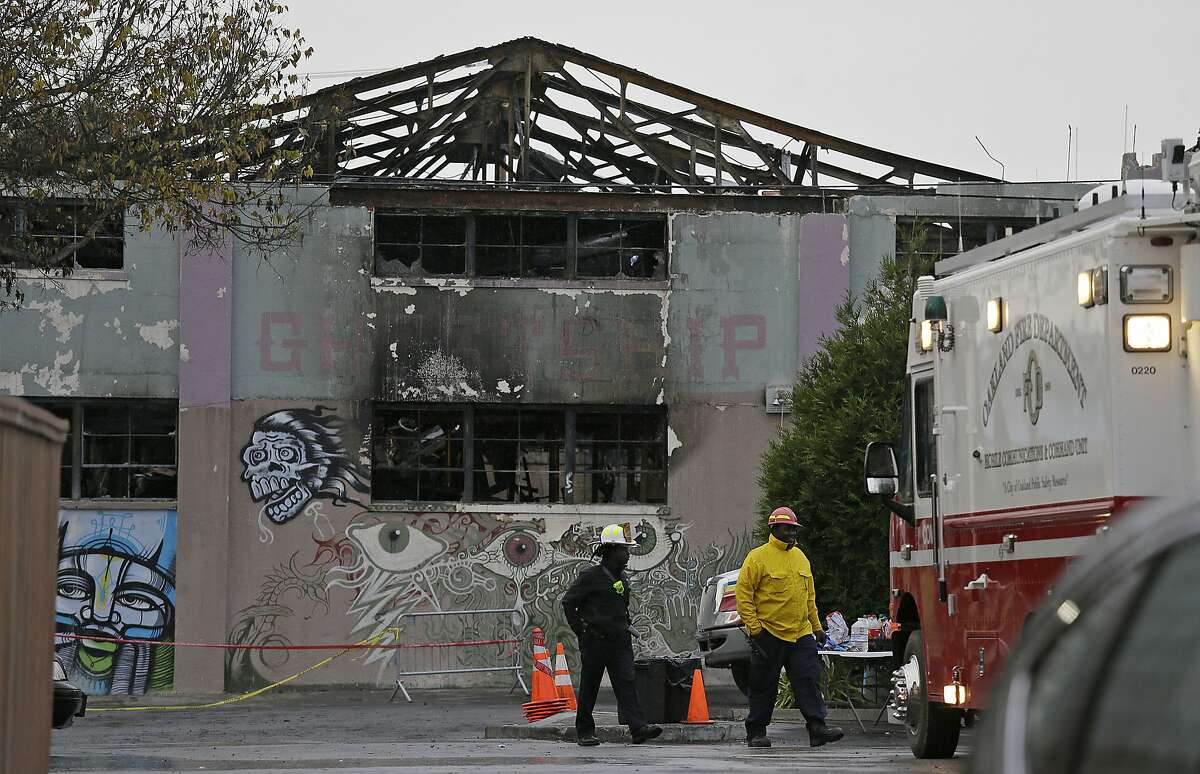 FILE - In this Dec. 7, 2016, file photo, Oakland fire officials walk past the remains of the Ghost Ship warehouse damaged from a deadly fire in Oakland, Calif. More than two years after 36 people died in the fire, Derick Almena and Max Harris, the two men who face charges of involuntary manslaughter, will stand trial on charges that they allegedly illegally converted the industrial building into an unlicensed entertainment venue and artist live-work space. (AP Photo/Eric Risberg, File)