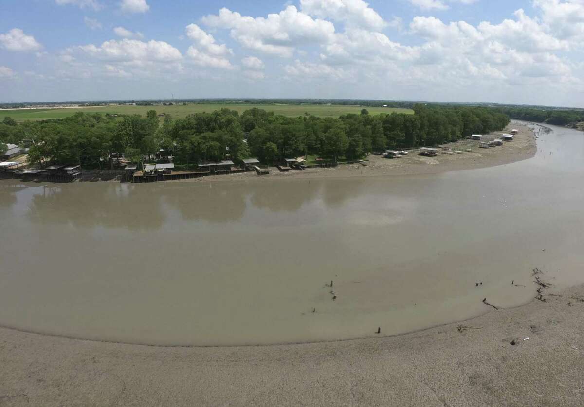 The draining of Lake Dunlap has left shallow, muddy water and exposed muddy banks. The lake was narrow before dam broke but now resembles a river channel.