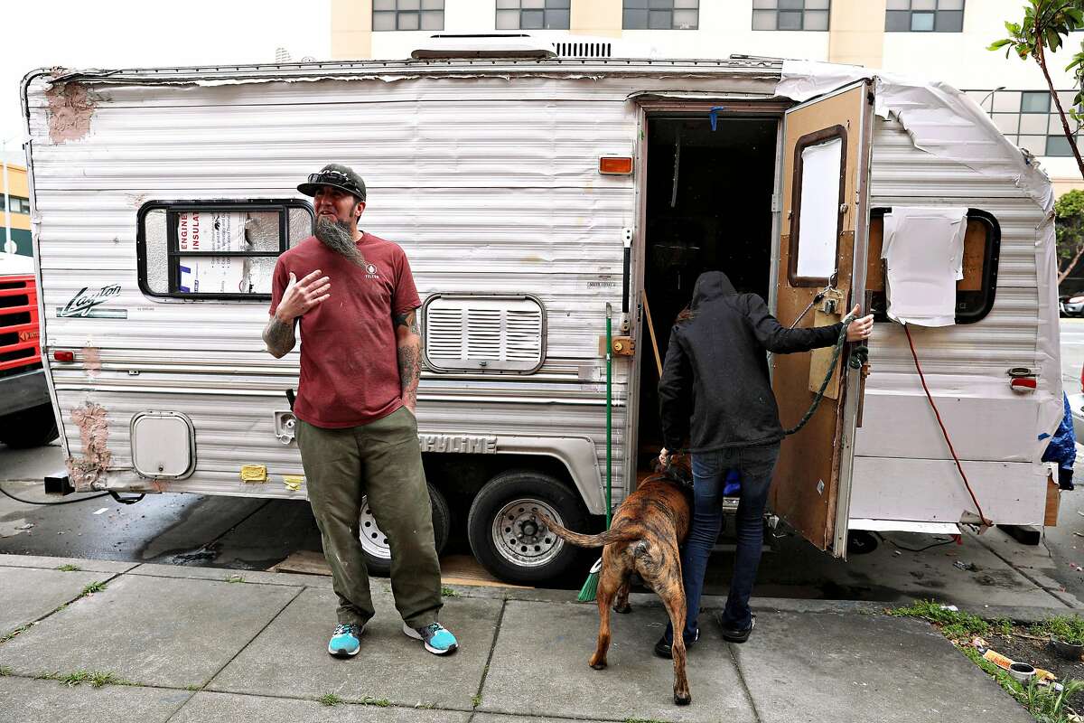 James Janisse (left) stands outside the travel trailer he lives in as his wife Lisa Janisse (right) returns from walking their dog, Kodiak (center), on Thursday, May 16, 2018 in San Francisco, Calif.