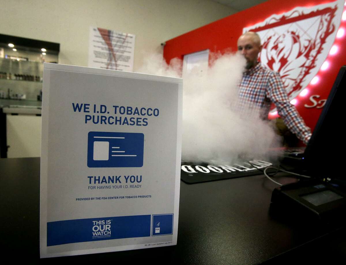 A sign on the counter at the Smoke to Live vape shop at 18154 Blanco Road reminds customers Thursday April 19, 2018 that tobacco products cannot be sold to people under the age of 18. Retailers, convenience stores, and smoke shop owners are preparing for the October 1 implementation of San Antonio's ordinance raising the tobacco buying age to 21. Vaping (right, background) is store manager Jordan Studer.