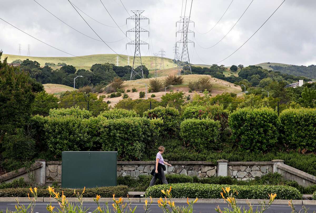 A woman walks underneath high-voltage power transmission lines owned by PG&E stretched across a neighborhood near San Ramon Valley Boulevard in San Ramon, Calif. Friday, May 17, 2019.