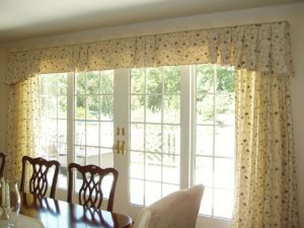 A transitional valance is paired with coordinating draperies, both from Laura’s Draperies, Bedspreads & More in Norwalk, resulting in a warm, inviting dining room. — Laura’s Draperies, Bedspreads & More photo