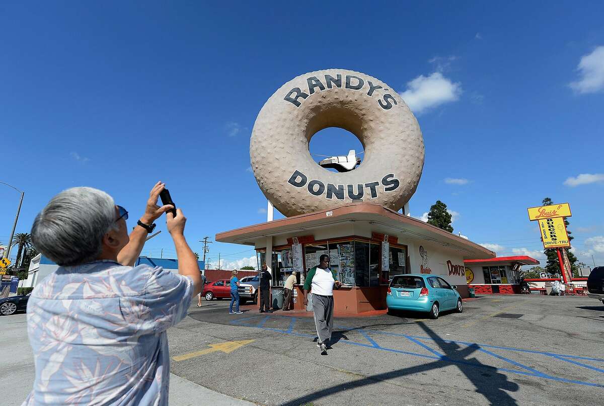 LOS ANGELES, CA - OCTOBER 10: A man takes a picture with his mobile phone of a toy space shuttle placed in the dounut hole of Randy's Donuts in preparation of the ground transport of the space shuttle Endeavour on October 10, 2012 in Los Angeles, California. The orbitor will stop in front of the donut shop for several hours to shoot a Toyota commercial. The space shuttle will start its trek from the Los Angeles International Airport to the California Science center on Friday. (Photo by Kevork Djansezian/Getty Images)