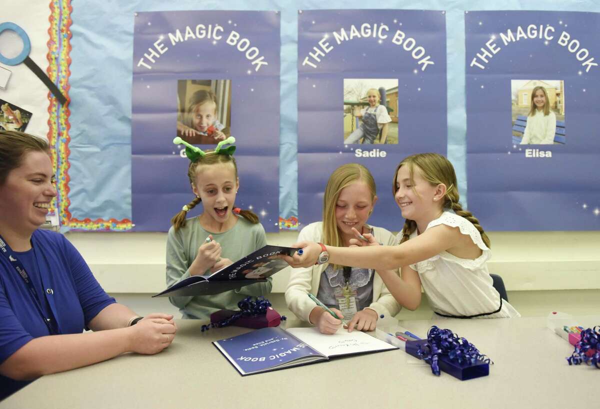 Teacher Amanda Kocot gets her copy of "The Magic Book" signed by fourth-grader authors Gabriela Gigliani, left, Sadie Hasen, center, and Elisa Infante during the book reading and performance of "The Magic Book" at Old Greenwich School in Old Greenwich, Conn. Monday, May 20, 2019. Fourth-graders Gabriela Gigliani, Sadie Hasen, and Elisa Infante recently published "The Magic Book" and unveiled it Monday with a reading to a class of preschoolers. In the book, an alien meets a horse-human and they travel to Old Greenwich School in search of new body parts, only to discover that all they really needed was love.