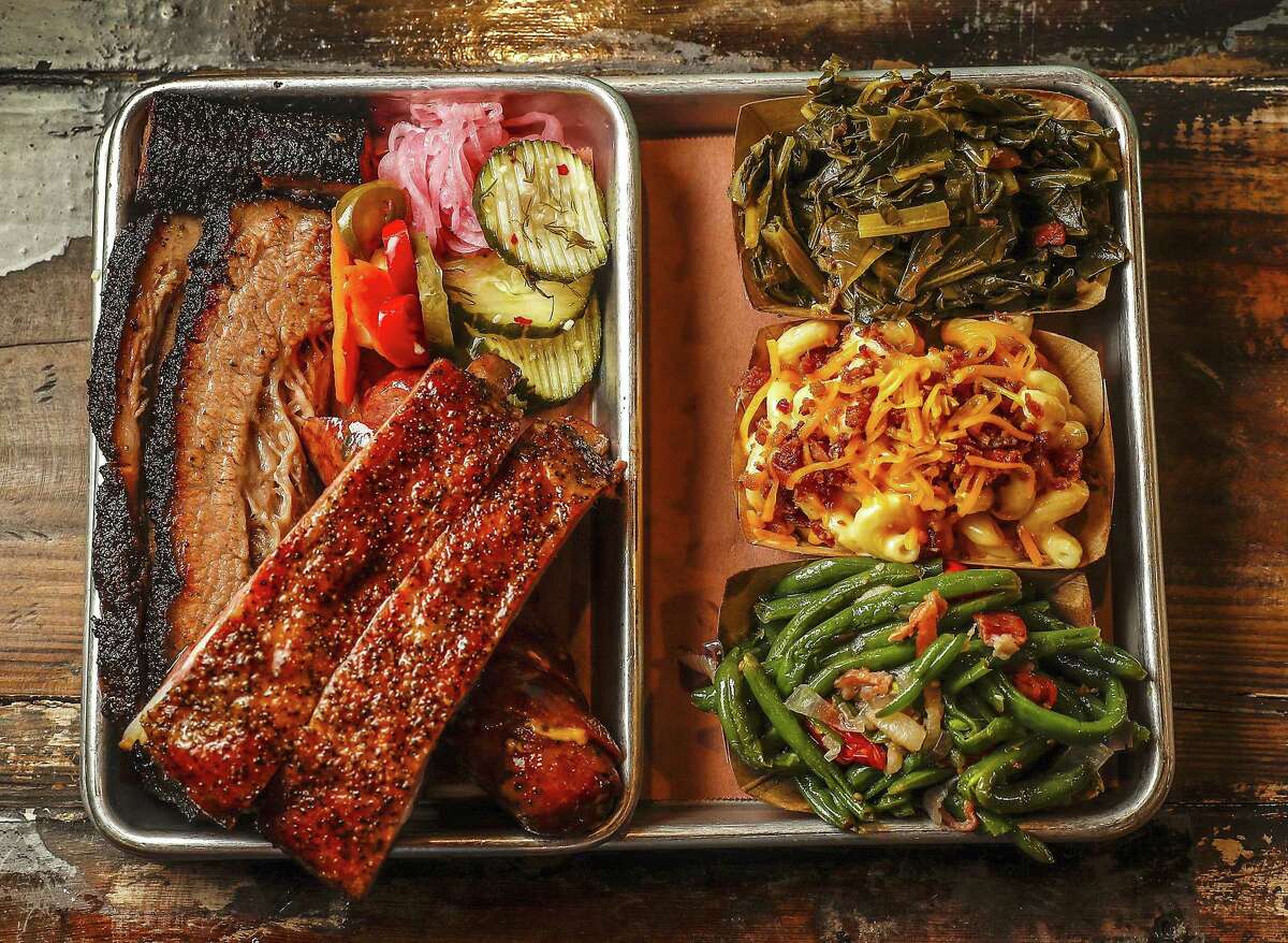 Three-meat tray with moist brisket, pork ribs, and jalapeño sausage served with sides of collard greens, green beans with tomatoes and onions, and mac and cheese with bacon and cheddar cheese, along with pickles, pickled onions and escabeche at Truth BBQ