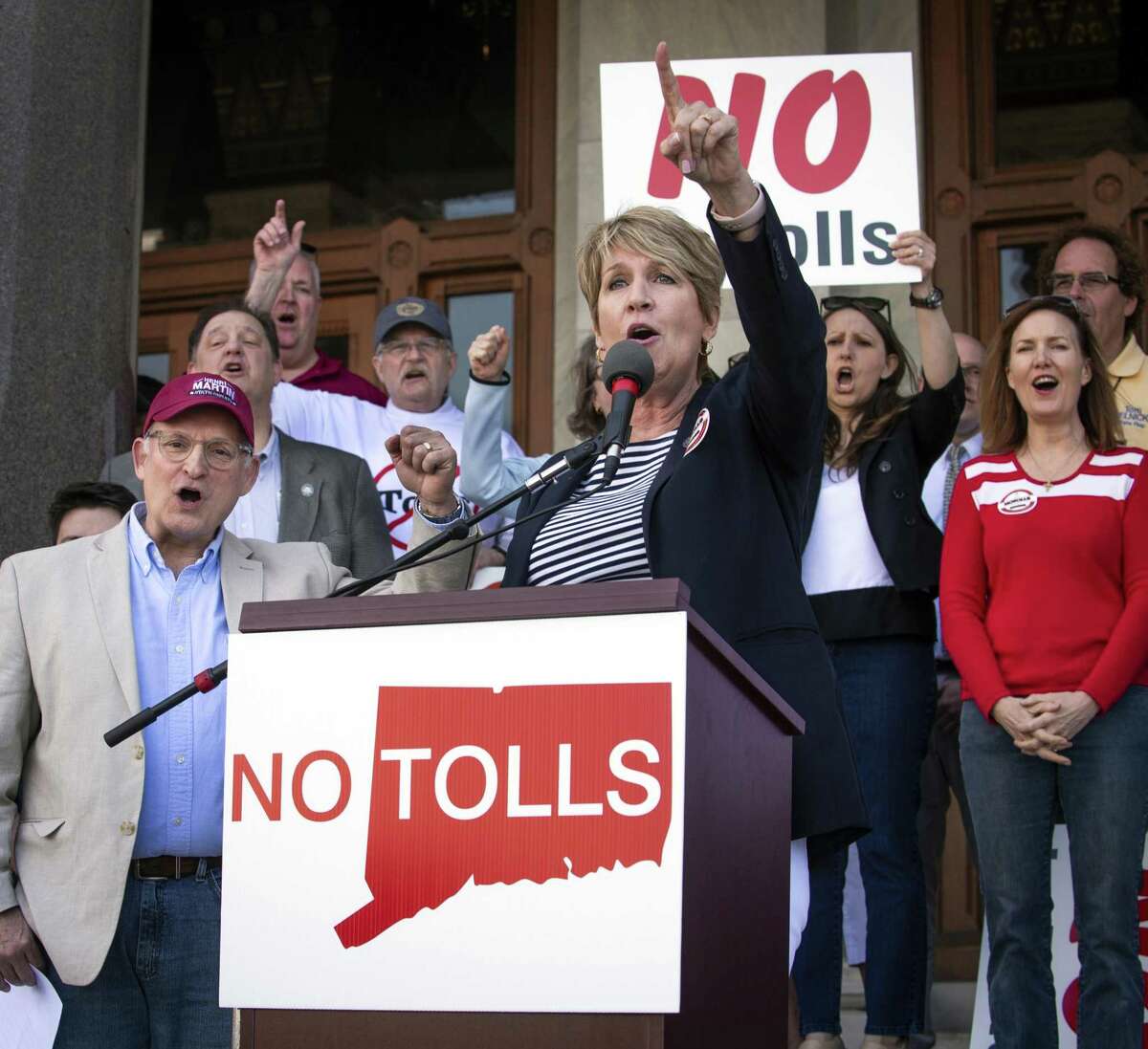 State Rep. Laura Devlin addresses the crowd of anti-toll protesters in front of the Capitol Building, Saturday, May 18, 2019 in Hartford, Conn. Protesters have gathered outside the state Capitol to rally against a proposal to put electronic tolls on the state's highways. Demonstrators on Saturday called the plan another tax increase state residents can't afford. They held "no tolls" signs and wore "no tolls" shirts as they criticized Democratic Gov. Ned Lamont's plan to raise money for highway improvements.(Melanie Stengel/Hartford Courant via AP)