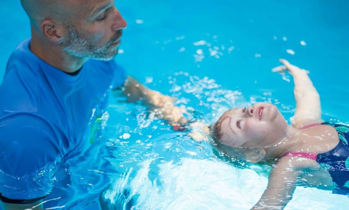 A survival swimming instructor teaches a child how to float in a pool.