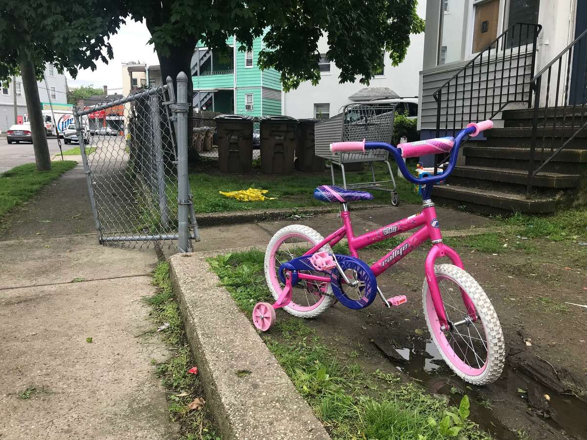 A child’s bicycle stands next to discarded police caution tape at a Stamford residence on Frederick Street where a man was killed on Wednesday, May 21, 2019.