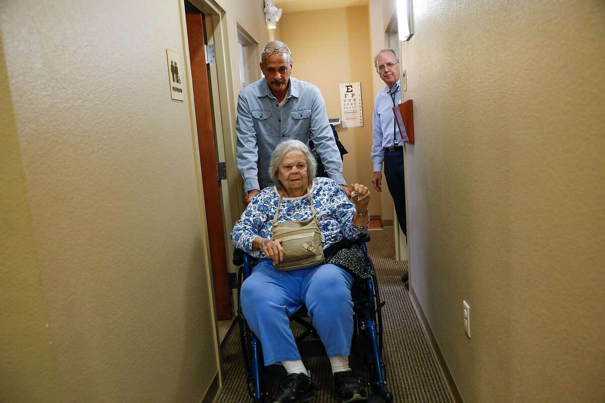 Jay Alexander wheels his mother Barbara Alexander, 80 (center) down the hallway after Dr. Richard Turner (right) saw her for an appointment at Paradise Medical Group in Paradise, California, on Thursday, May 23, 2019. Paradise Medical Group, the largest independent medical provider in Paradise, is reopening its primary care center this week after being closed due to the Camp Fire.
