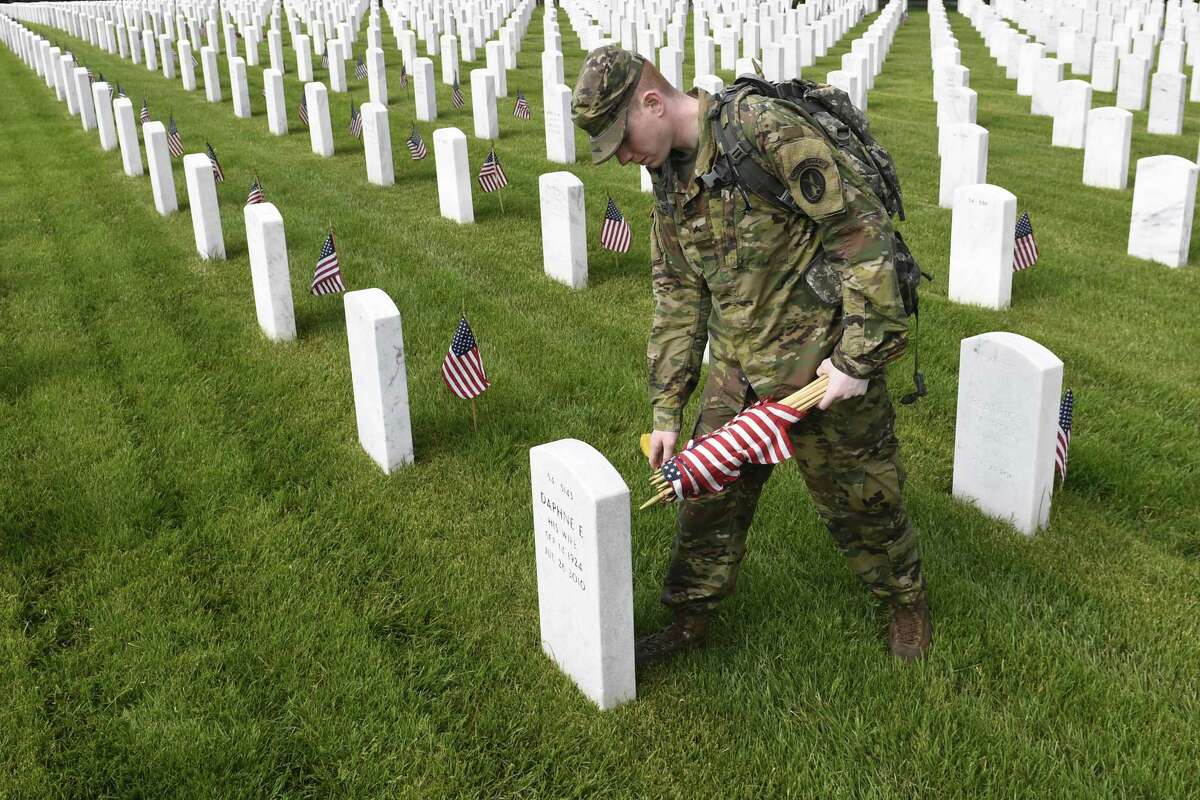 Army Cpl. Matthew Munie, of Jackson, Mich., and a member of the 3d U.S. Infantry Regiment also known as The Old Guard, places flags in front of a headstone for “Flags-In” at Arlington National Cemetery in Arlington, Va., Thursday, May 23, 2019, to honor the nation’s fallen military heroes.