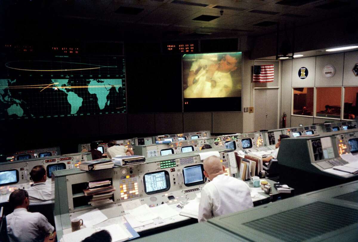 This photograph of the Mission Operations Control Room in the Mission Control Center at the Manned Spacecraft Center (now Johnson Space Center) in Houston, was taken on April 13, 1970, during the fourth television transmission from the Apollo 13 mission. Gene Kranz (foreground, back to camera), one of four Apollo 13 flight directors, views the large screen at front as astronaut Fred W. Haise Jr., the lunar module pilot, is seen on the screen.