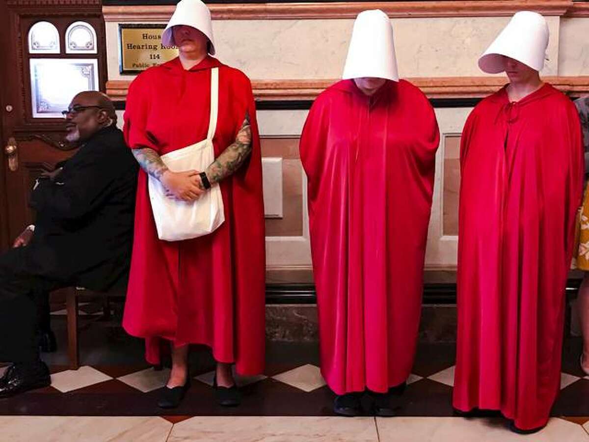 Women dressed as Handmaids, characters from Margaret Atwood’s dystopian novel, “The Handmaid’s Tale,” stand by as House Democrats meet on the other side of the door to discuss the future of the Reproductive Health Act on Wednesday at the Capitol in Springfield.