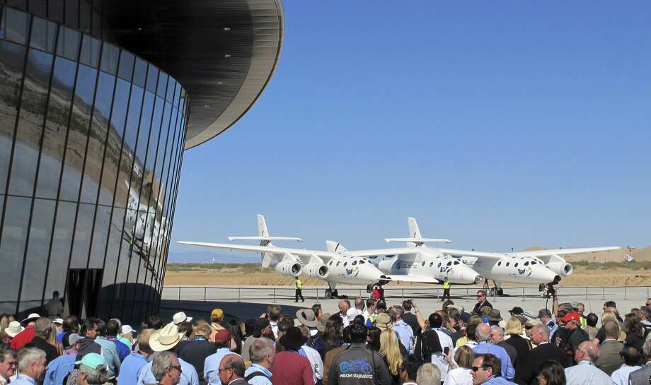 In this Oct. 17, 2011 photo a crowd gathers outside Spaceport America for a dedication ceremony as Virgin Galactic's custom-built jet aircraft WhiteKnightTwo and its spacecraft SpaceShipTwo sit on the tarmac near Upham, N.M. British billionaire Richard Branson is taking another concrete step toward offering rides into the close reaches of space for paying passengers. Branson announced Friday, May 10, 2019, that Virgin Galactic will immediately begin shifting operations from California to a spaceport and specialized runway in the New Mexico desert in final preparations for commercial flights. He says Virgin Galactic's development and testing program has advanced enough to make the move, which will continue through the summer. (Associated Press)