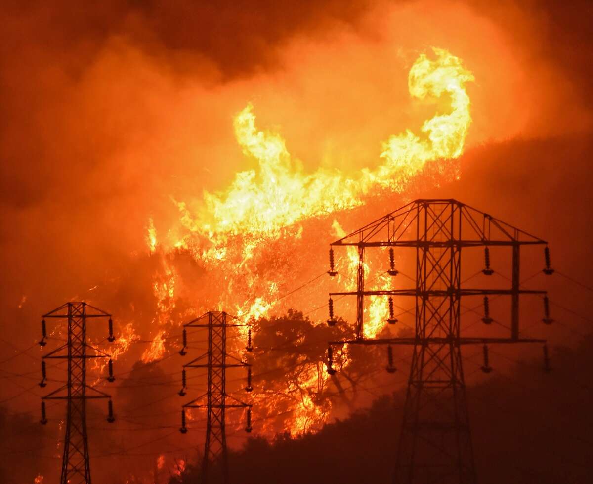 FILE - In this Dec. 16, 2017, file photo provided by the Santa Barbara County Fire Department, flames burn near power lines in Sycamore Canyon near West Mountain Drive in Montecito, Calif. State fire officials blame Pacific Gas & Electric Corp.'s equipment for starting more than a dozen California wildfires over the last two years. PG&E filed for bankruptcy in Jan. 2019, saying it faced at least $13 billion in legal claims from wildfire victims. (Mike Eliason/Santa Barbara County Fire Department via AP, File)