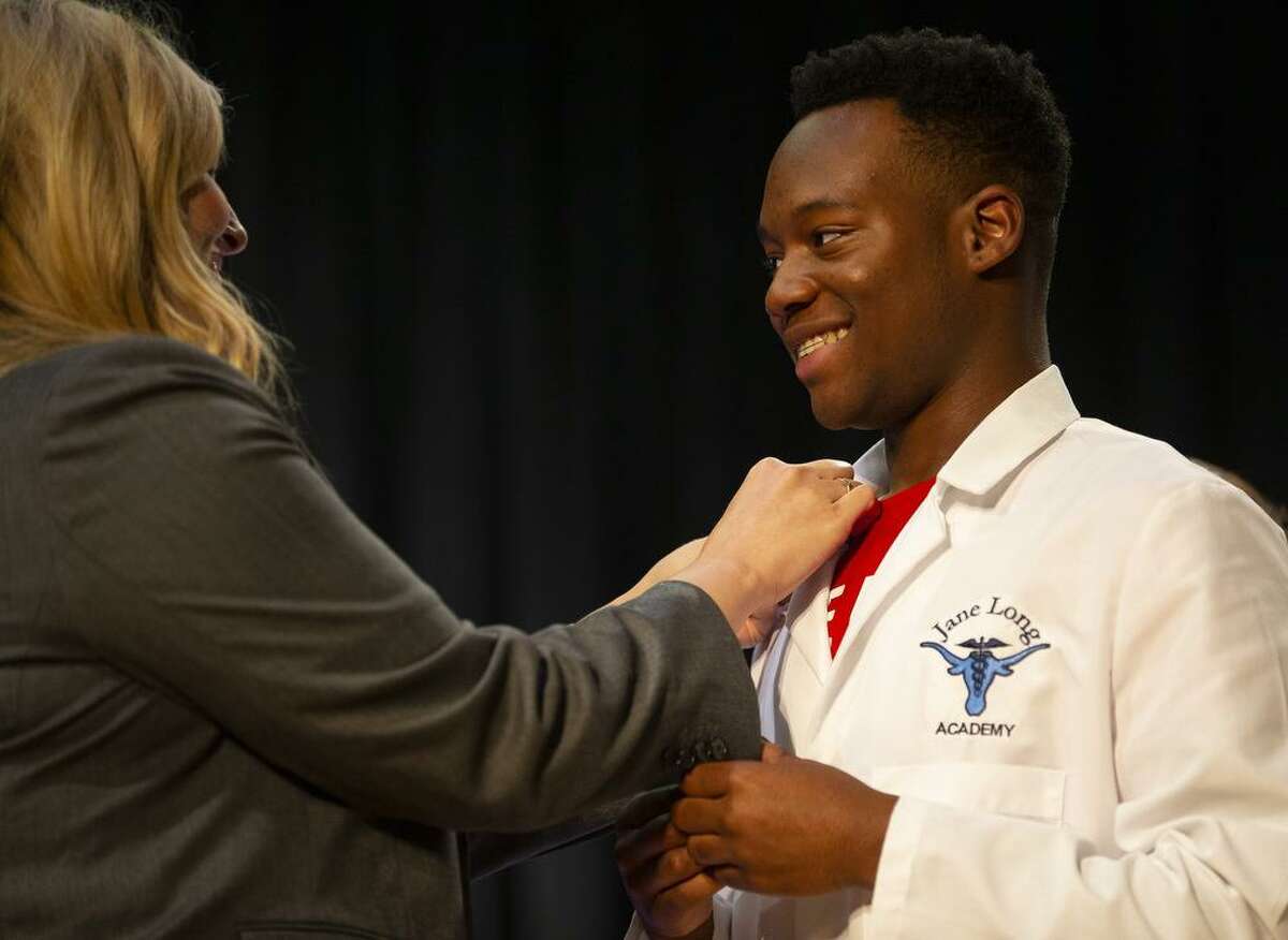 Student Cameron Simon receives a pin from principal Keri Wittpenn during Jane Long Academy's annual White Coat Ceremony in the school's auditorium, Wednesday, May 22, 2019. The HISD school specializes in preparing students for careers in the medical field, specifically as pharmacy techs and medical coders. During the White Coat Ceremony, juniors and seniors present the freshman and sophomores their white coats.