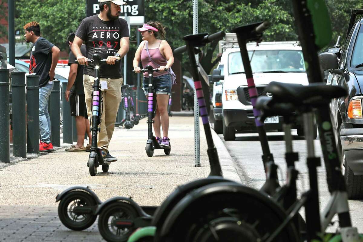 Jose Velasquez, left, and Joanna Escobedo, here in San Antonio from the Valley on vacation, ride scooters on the side walk on Presa Street. The City Council voted to ban riding scooters on sidewalks by June 30.