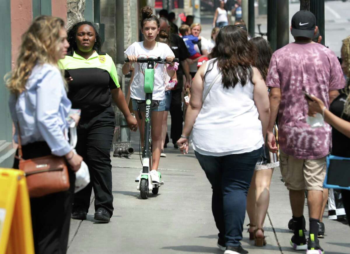 A young girl rides a scooter on a crowded side walk on Commerce Street on Thursday, May, 30, 2019. The City Council voted to ban riding scooters on sidewalks by June 30.