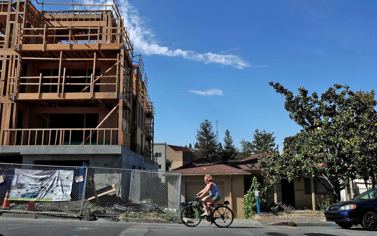 A cyclist rides by new, luxury condo construction next to a single-family home on Trinity Avenue in Walnut Creek, Calif., on Sunday, May 5, 2019. State Sen. Scott Wiener's SB50, besides allowing denser housing near transit, would wipe out single-family zoning in many suburban cities and allow apartment construction in such areas.