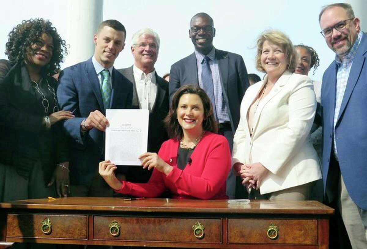 AP FILE PHOTO - Michigan Gov. Gretchen Whitmer, seated, displays the auto insurance legislation she signed in 2019 at the Detroit Regional Chamber's Mackinac Policy Conference at the Grand Hotel on Mackinac Island. Whitmer signed the overhaul of Michigan's car insurance system which will let drivers forego unlimited medical benefits to cover crash injuries, and declared it an 'historic day' because the cost of auto insurance will go down.