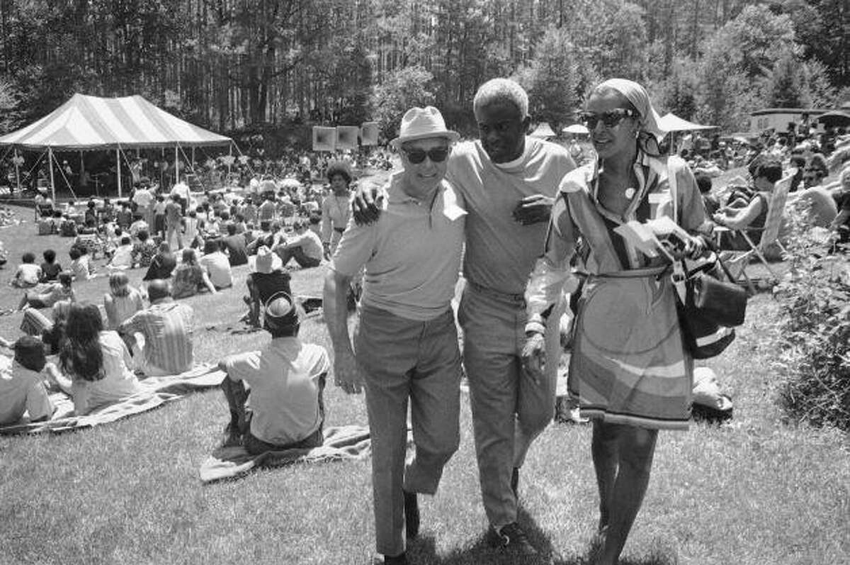 Jackie Robinson, baseball legend, walks with an unidentified friend (left) and Mrs. Arthur Logan, a family friend, at a Jazz Concert at the Robinson home on June 27, 1971 in Stamford, Connecticut. The concert was originally planned by Jackie Robinson Jr., for a drug rehabilitation center. The younger Robinson was killed in an auto accident.