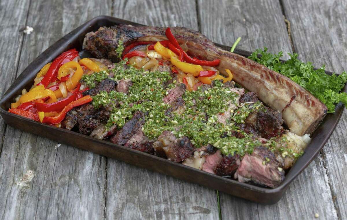 The finished presentation of two tomahawk steaks with grilled peppers and onions and topped with chimichurri.