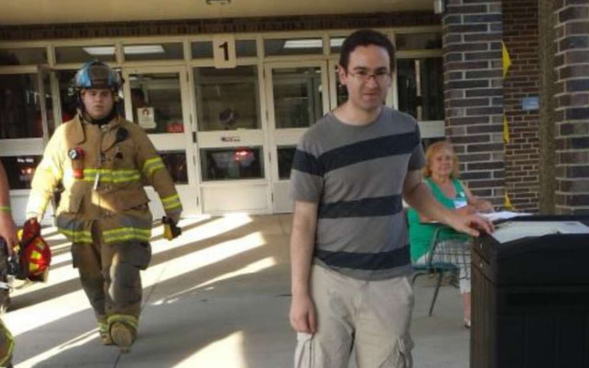 Mike Newman casts his ballot during the fire alarm at Hillcrest Middle School as firefighters exit the building.
