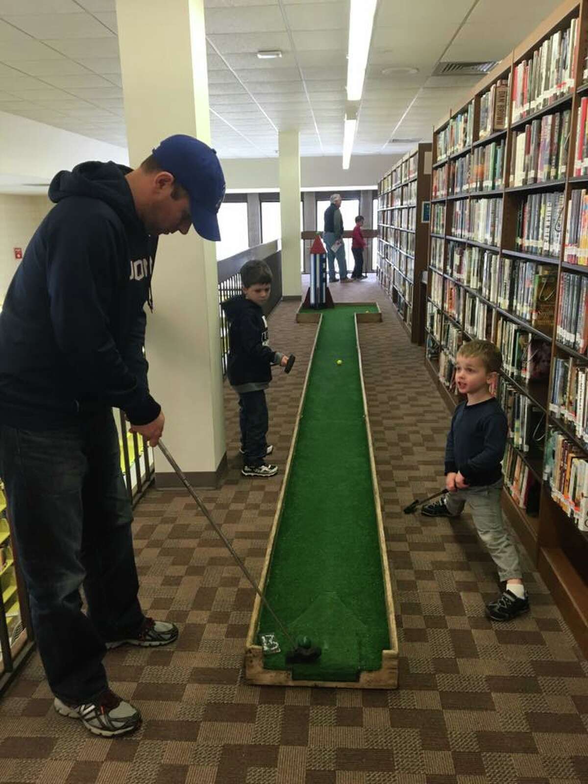 A father teacher his son how to put at one of the 18 holes set up at the Trumbull Library Monday afternoon.