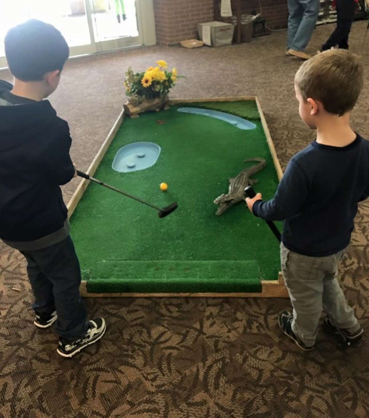 After studying the course, two sons of IMPACTrumbull prepare to put at one of the 18 holes that were set up at the Trumbull Library Monday afternoon.