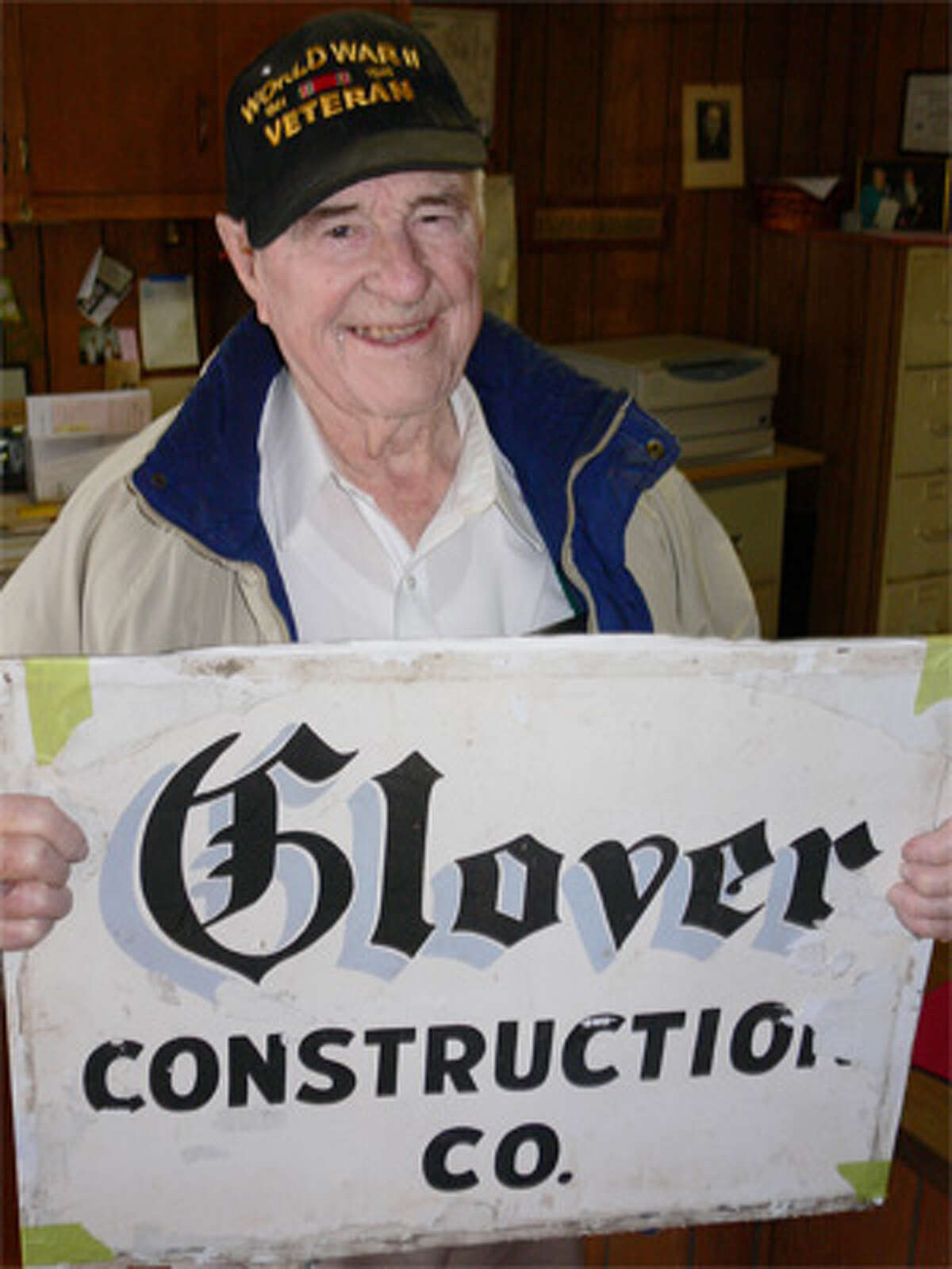 Leroy Glover, 92, holds a sign from the family construction company he ran in Shelton for many decades.