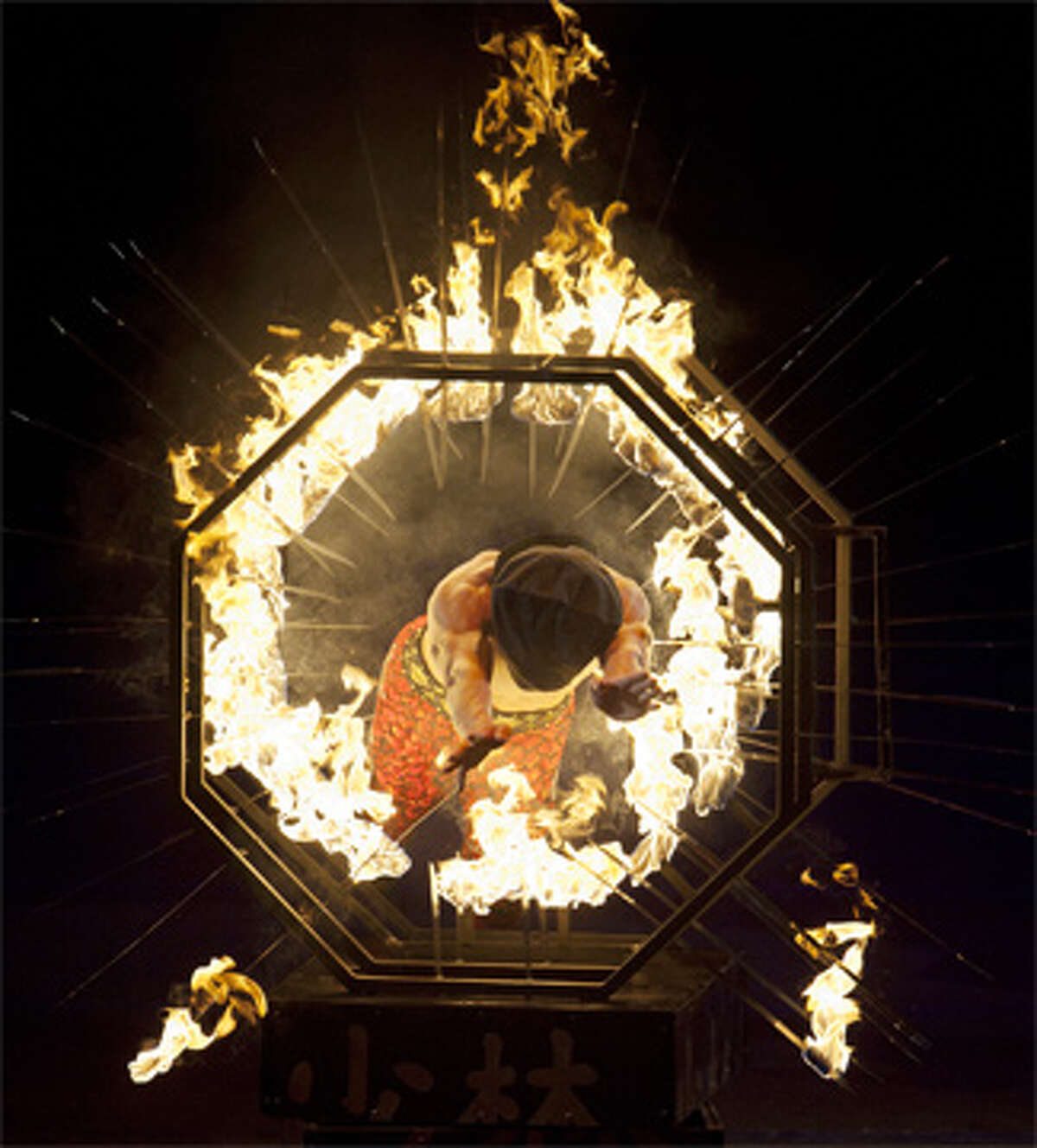 An aerial view of a Shaolin Warrior, or kung fu-style martial artist, jumping through knives on fire at a circus show.