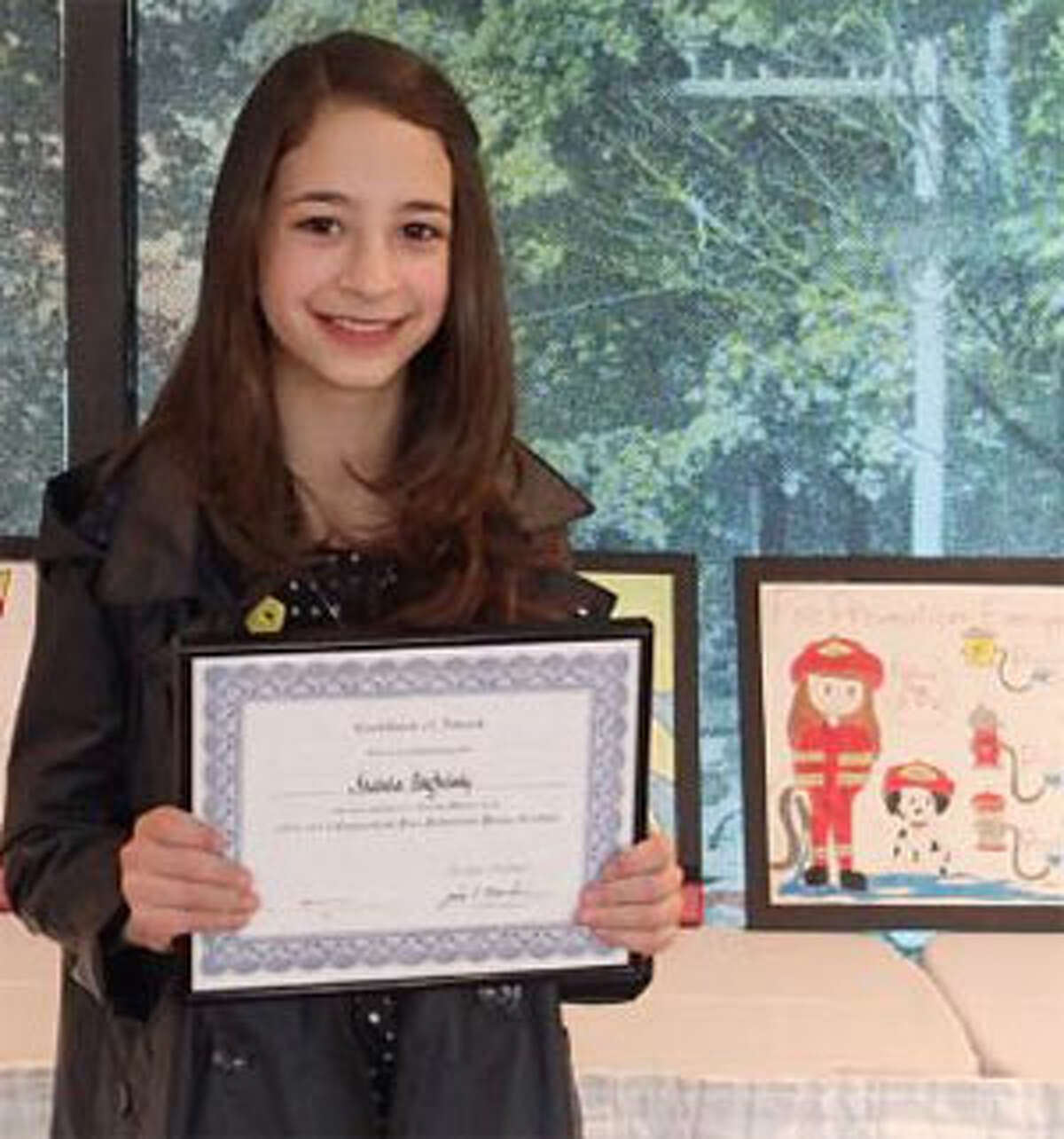 Isabela Baghdady, a St. Lawrence School fifth grader, holds her award certificate near the framed fire prevention poster she designed.